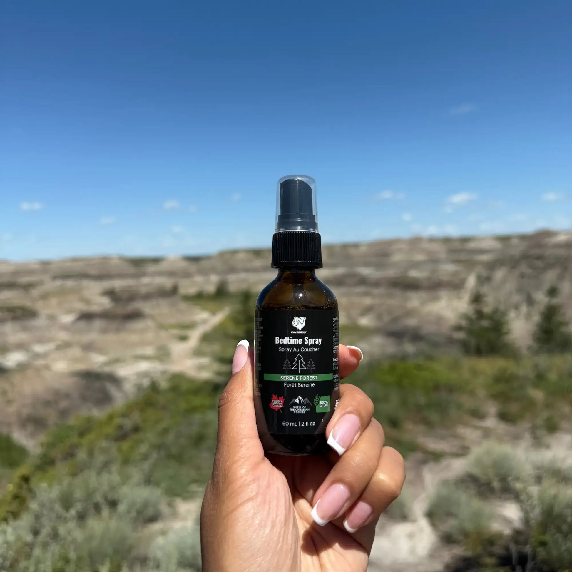 Girls hand holding a bottle of 'KAVEBROS Bedtime Spray' with a scenic background in Drumheller, AB